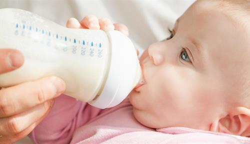 Photograph of a young baby being fed from a bottle by a bearded father