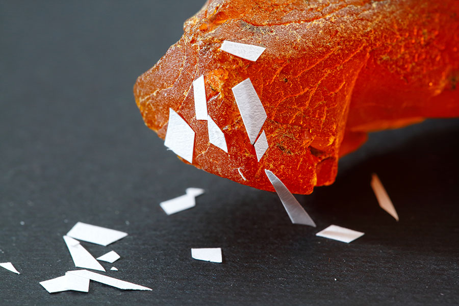 Photo shows a piece of amber with tiny pieces of paper clinging to it.