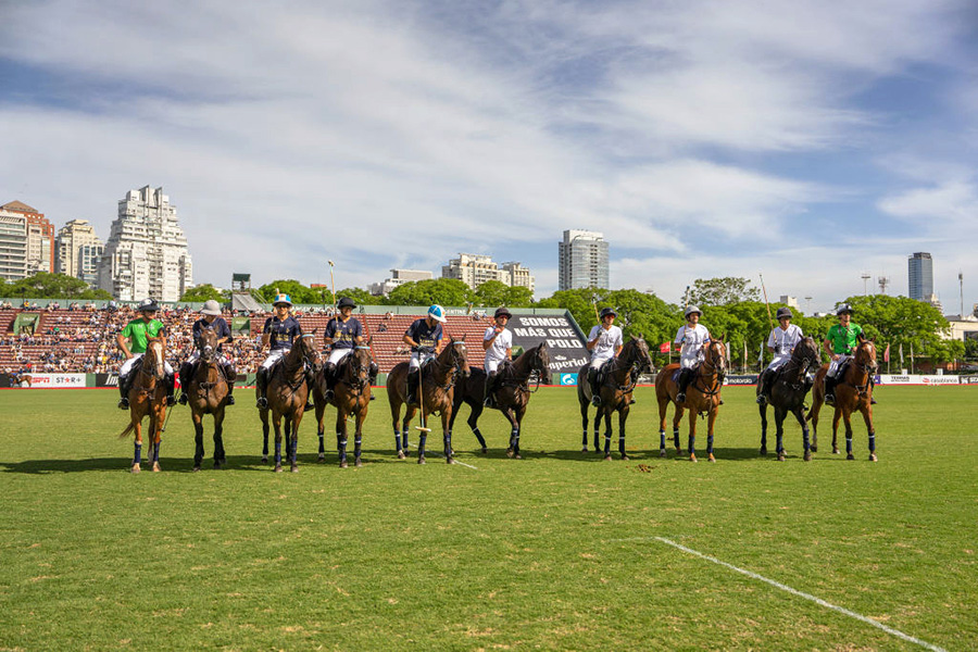 Ten horses with their riders lined up on a polo field.