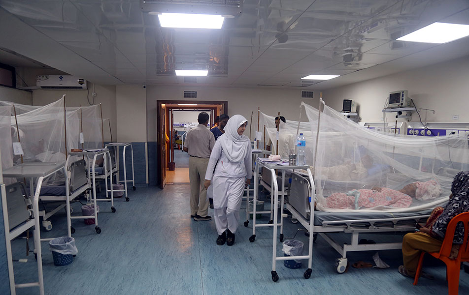 In a ward, patients lie in beds covered with netting, while health-care workers attend to them.
