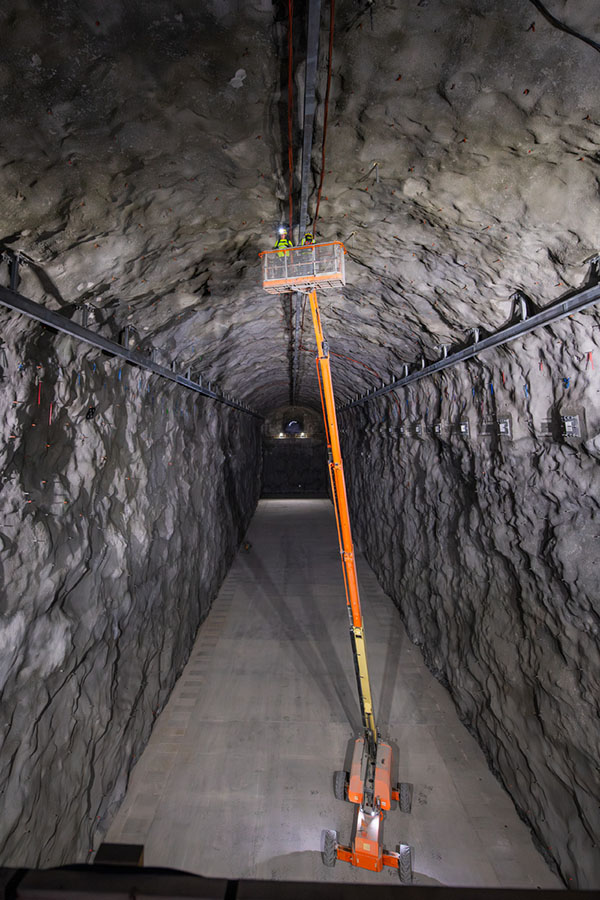 Workers on a hoist inspect the walls of a large tunnel.