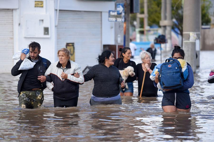 Photograph of people walking through a flooded street with water up to their thighs.