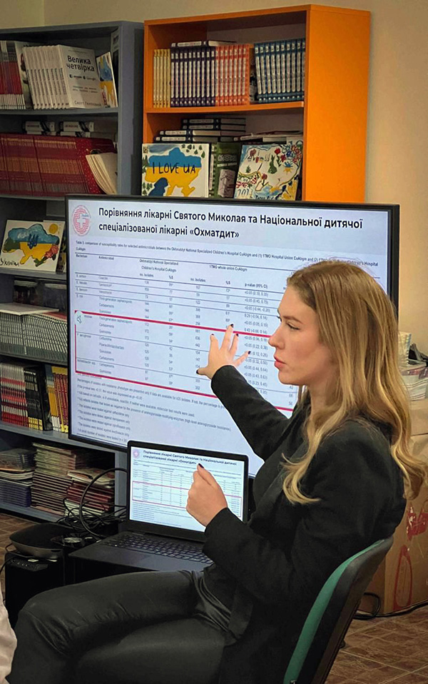A woman gestures at large screen showing a table of numbers.