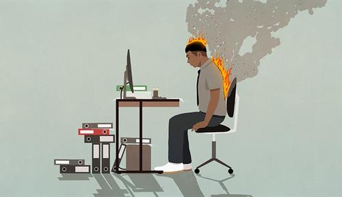 Conceptual illustration shows a man sitting at his office desk leaning forward. Files are heaped on the floor; a keyboard and monitor are on the desk. The man’s back is on fire and smoke is billowing off to the right.