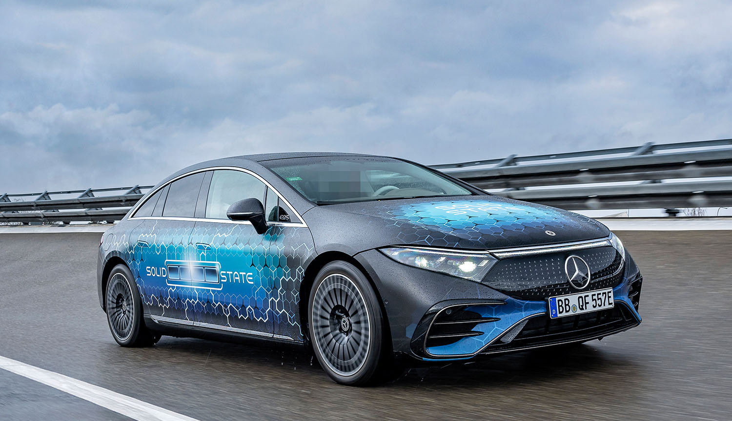 Photo from February 2025 shows a Mercedes-Benz car driving on a race track on a cloudy day. The car is covered with a design showing a charging battery and the words “Solid State.”