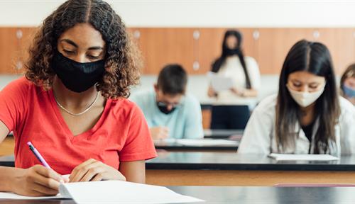 Photo shows Utah high school students returning to in-person learning in August 2020 during the Covid-19 pandemic. Students are seated far apart and wear face masks.
